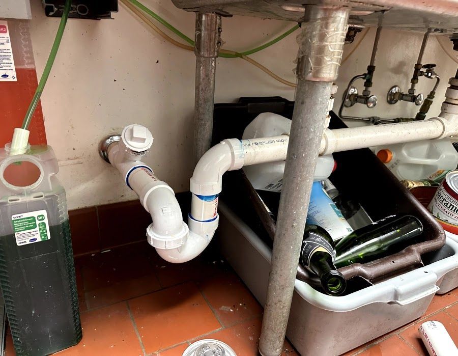 A sink with a pipe underneath it and a box of bottles underneath it.