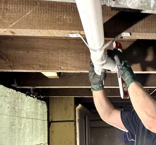 A man is working on a pipe under a wooden ceiling