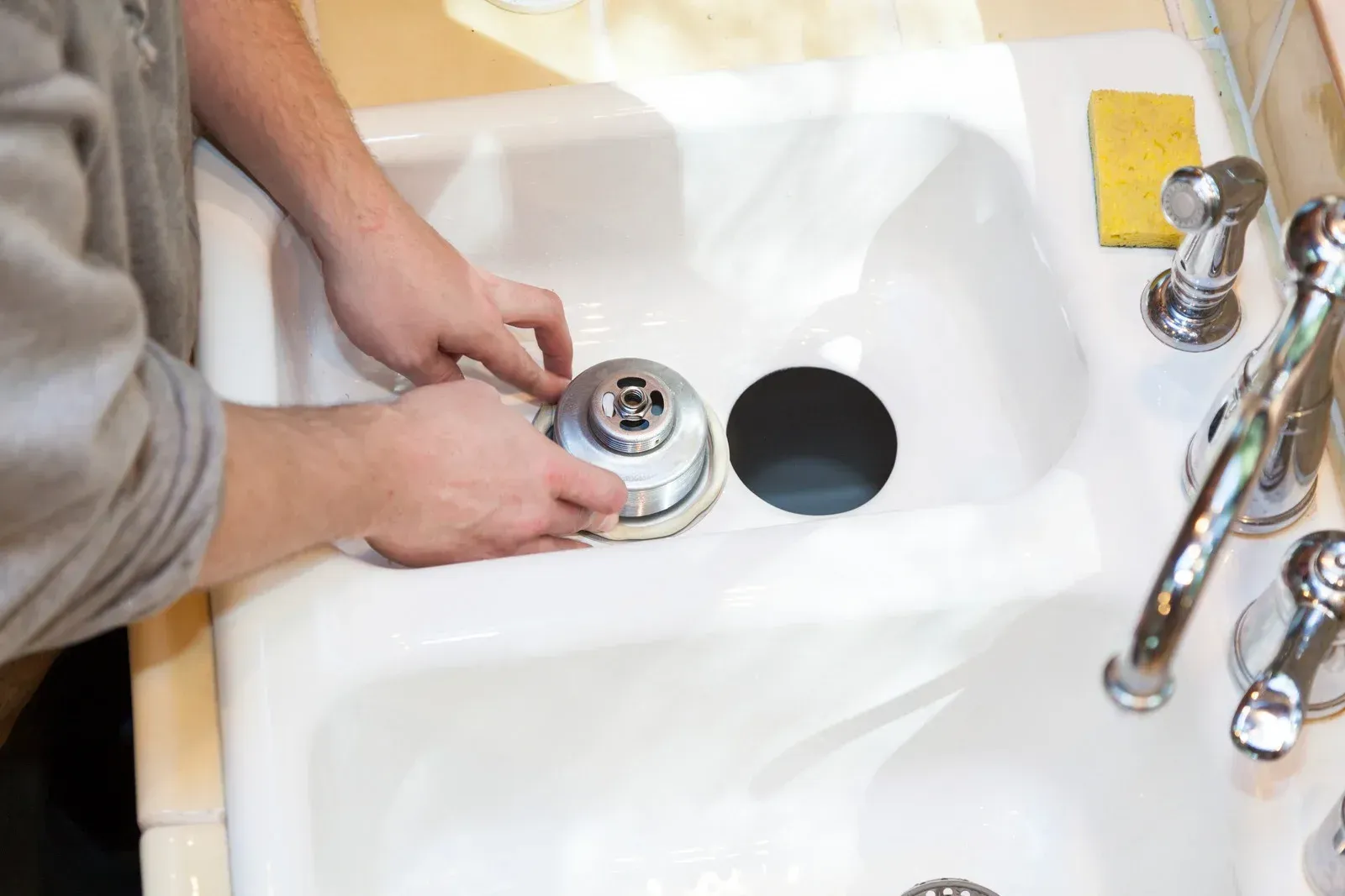 Person installing a sink drain in a white kitchen sink.
