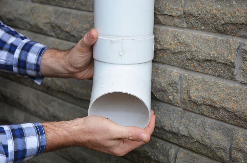 Person Connecting White Pvc Downspout to a Wall Outlet — Chris Murphy Plumbing & Maintenance In Langley Vale, NSW