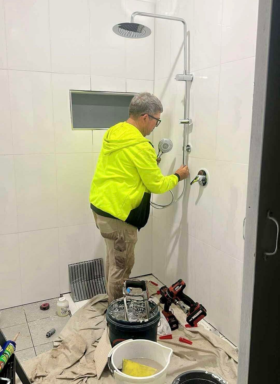 Person in Yellow Vest Installing Showerhead — Chris Murphy Plumbing & Maintenance In Langley Vale, NSW