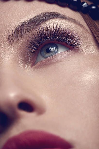 Hands applying eyelash extensions to a person's closed eye, with an eye pad in place. Pink tools are used.