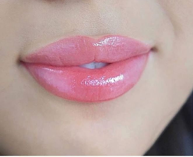 Close-up of full, glossy lips, colored with a light pink lipstick or gloss. The lips are slightly parted, revealing white teeth.