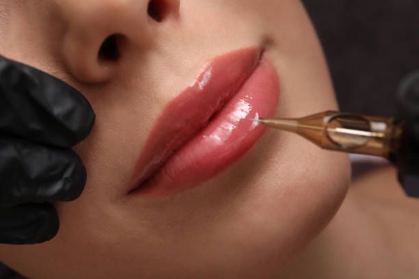 Lip blush procedure on full lips; a tattoo gun is used to apply color.