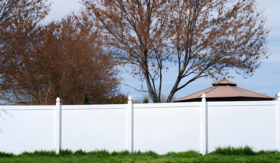 White vinyl privacy fence under autumn trees.