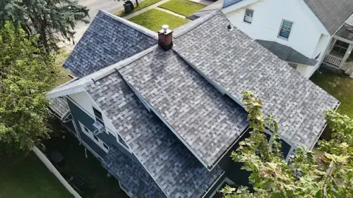 Aerial view of a gray shingled suburban house with a chimney and trees around it