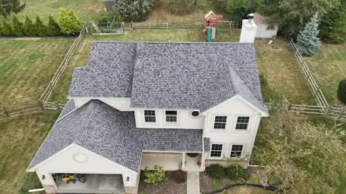 Aerial view of a white two-story house with gray roof, garage, and surrounding yard.
