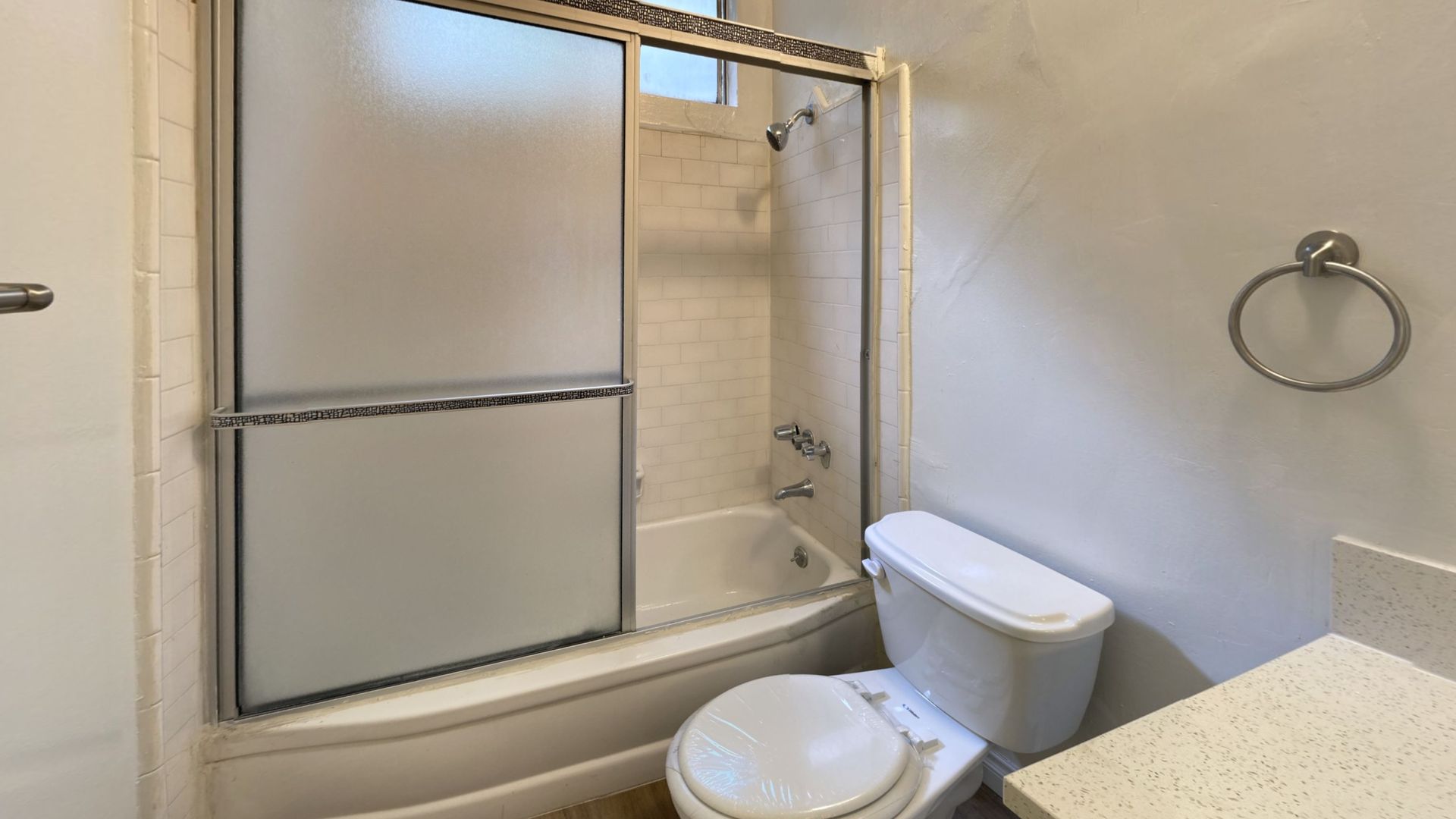 Bathroom with a white bathtub, toilet, and frosted glass shower door.