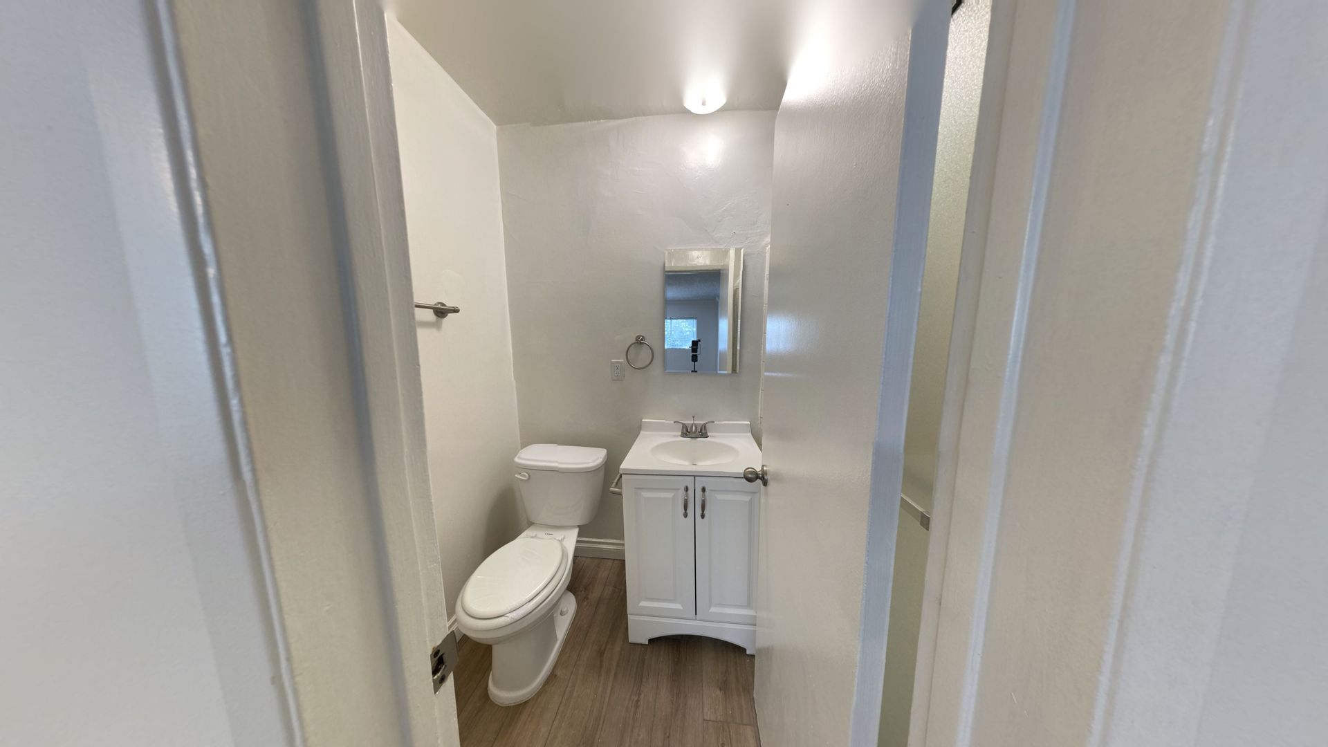 Small bathroom with a toilet, sink, and mirror. White walls and door frame.