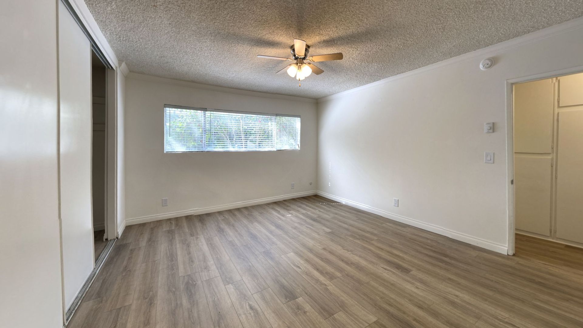 Empty room with light wood floors, window, ceiling fan, and white walls.
