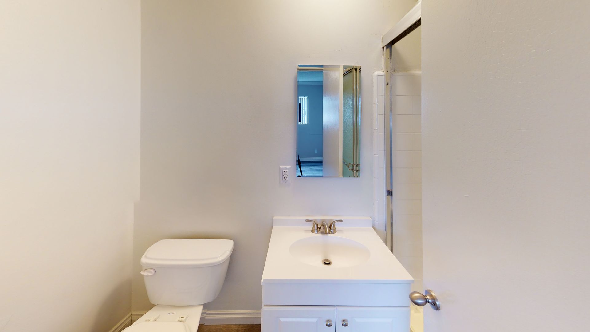 Bathroom with white toilet, vanity, mirror, and shower.