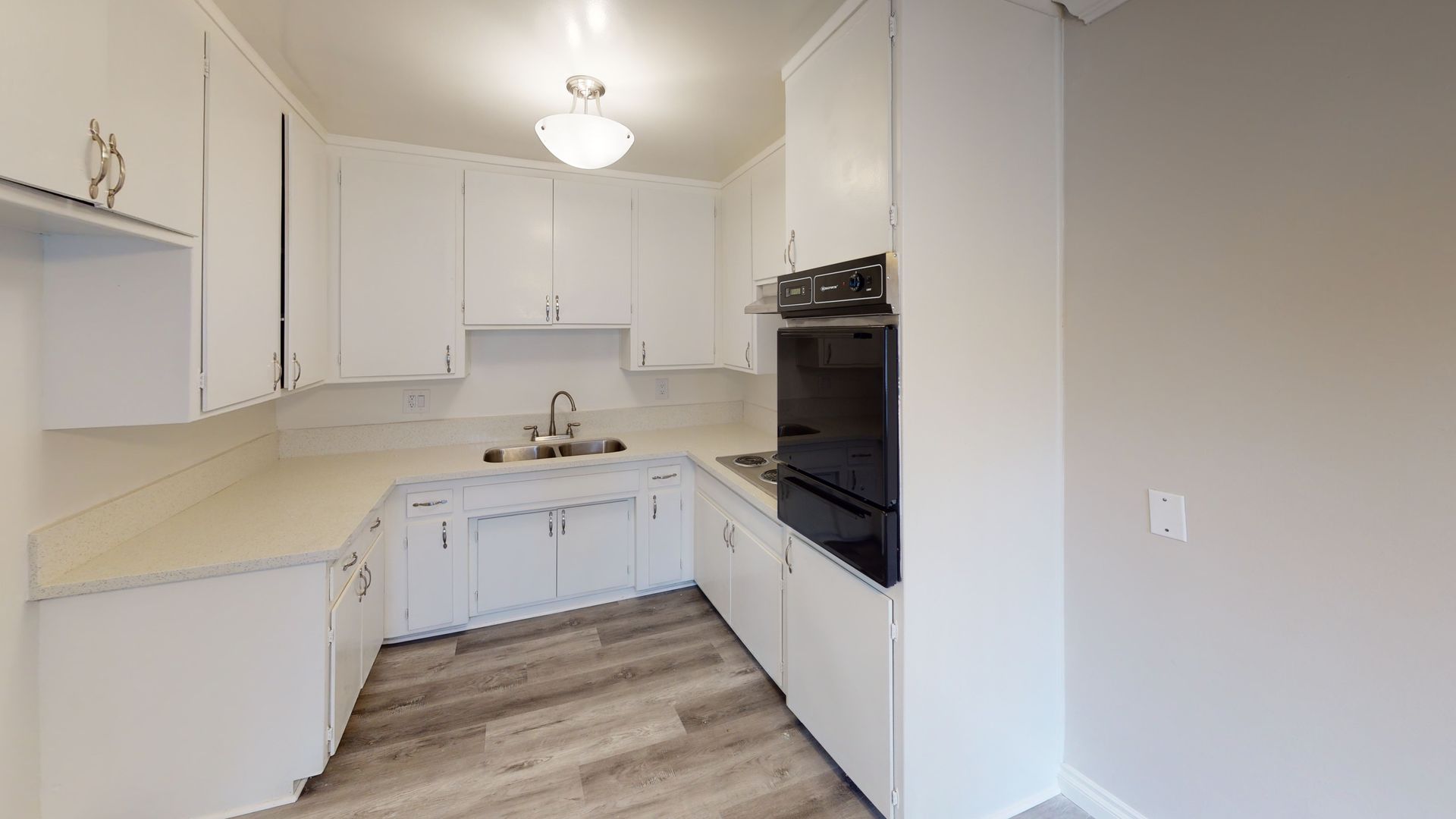 White kitchen with cabinets, countertops, and appliances; light wood-look flooring.