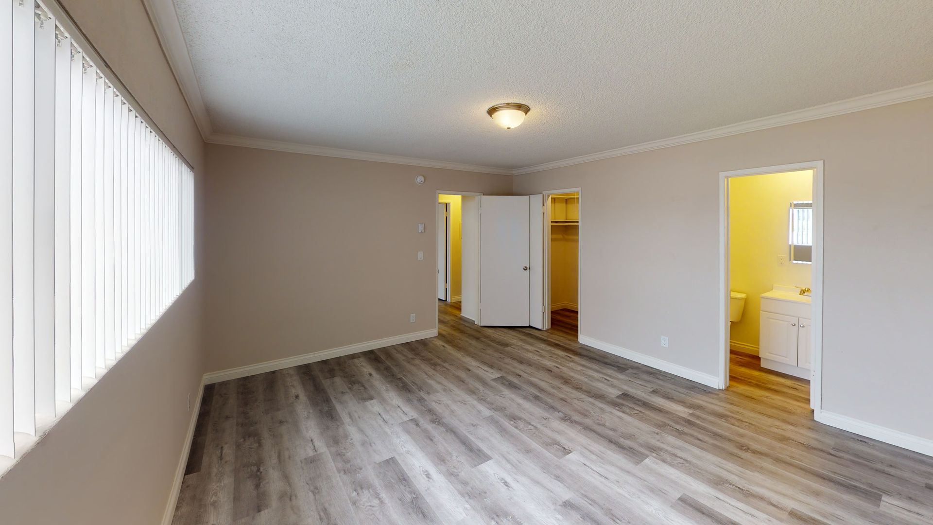 Empty room with wood-look flooring, large window with blinds, and doors to closet and bathroom.