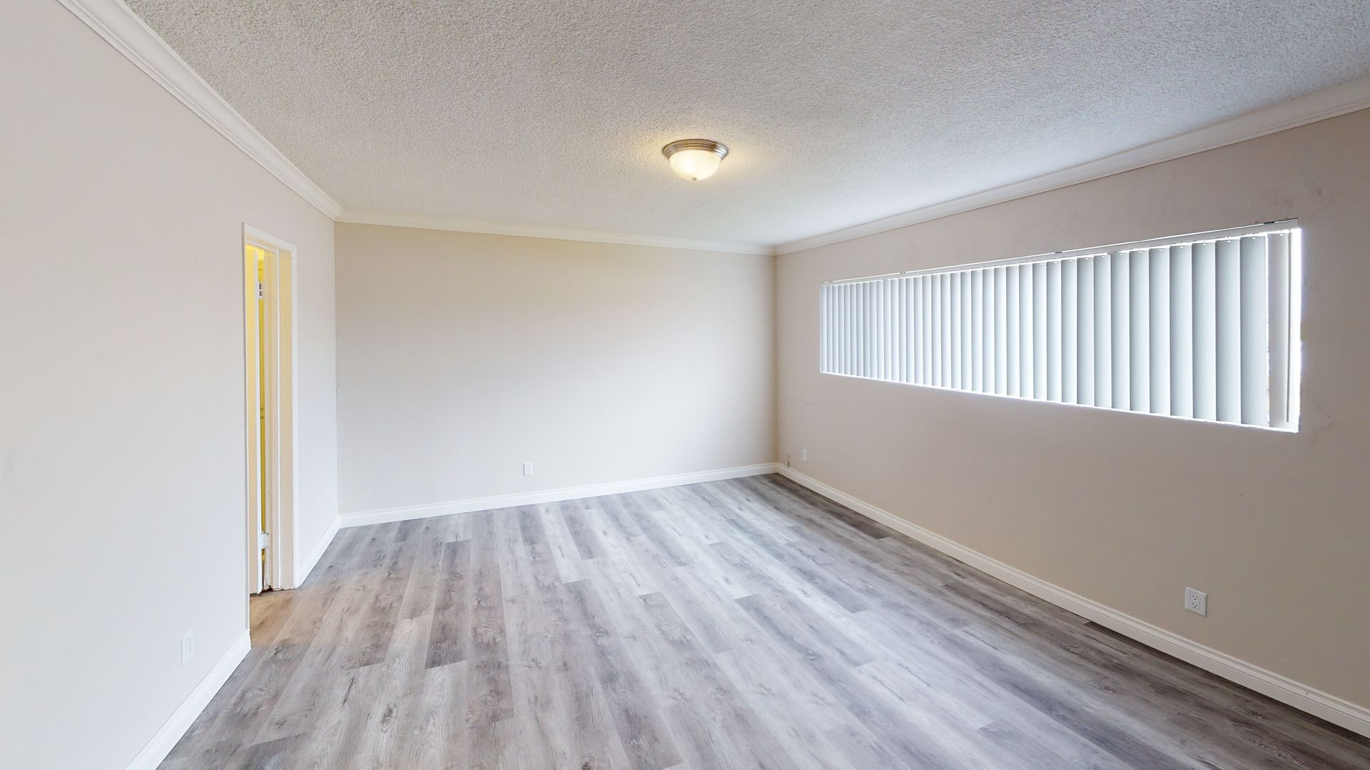 Empty room with gray wood-look floor, beige walls, and window with white blinds.