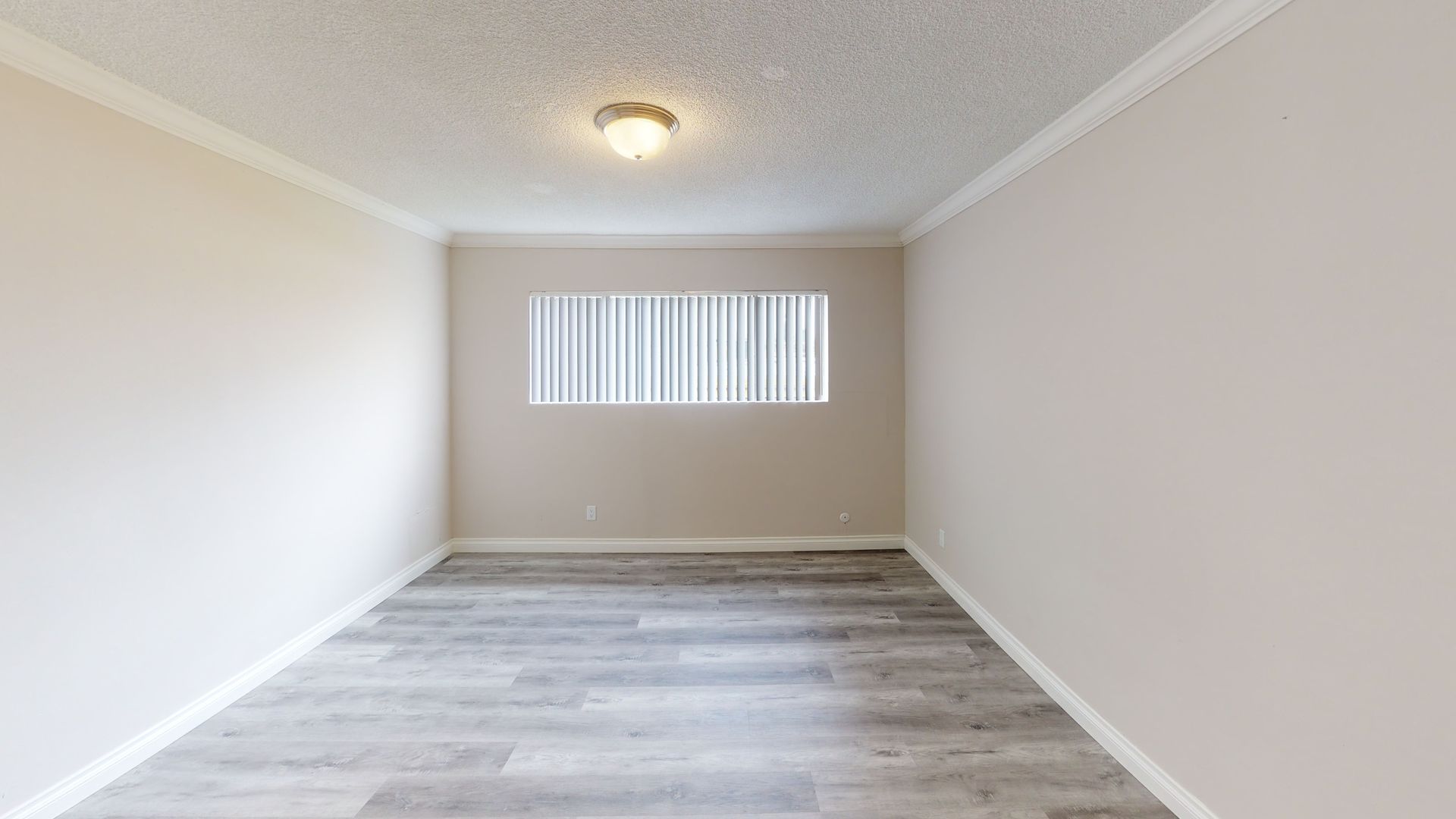 Empty room with light gray walls, window with blinds, and light wooden floor.