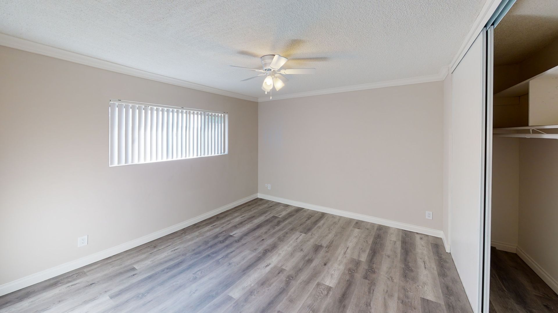 Empty bedroom with gray laminate flooring, window with blinds, and closet.