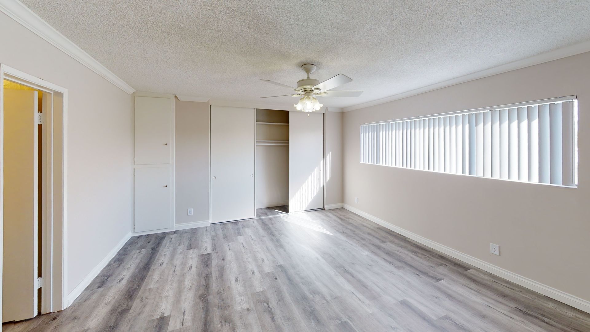 Empty bedroom with gray wood-look flooring, white walls, built-in closets, and window with blinds.