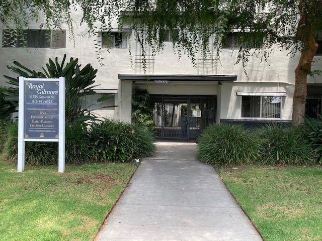 Apartment building entrance with sign, walkway, and greenery.