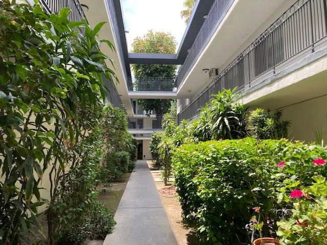 Apartment courtyard with a walkway lined with lush greenery and balconies.