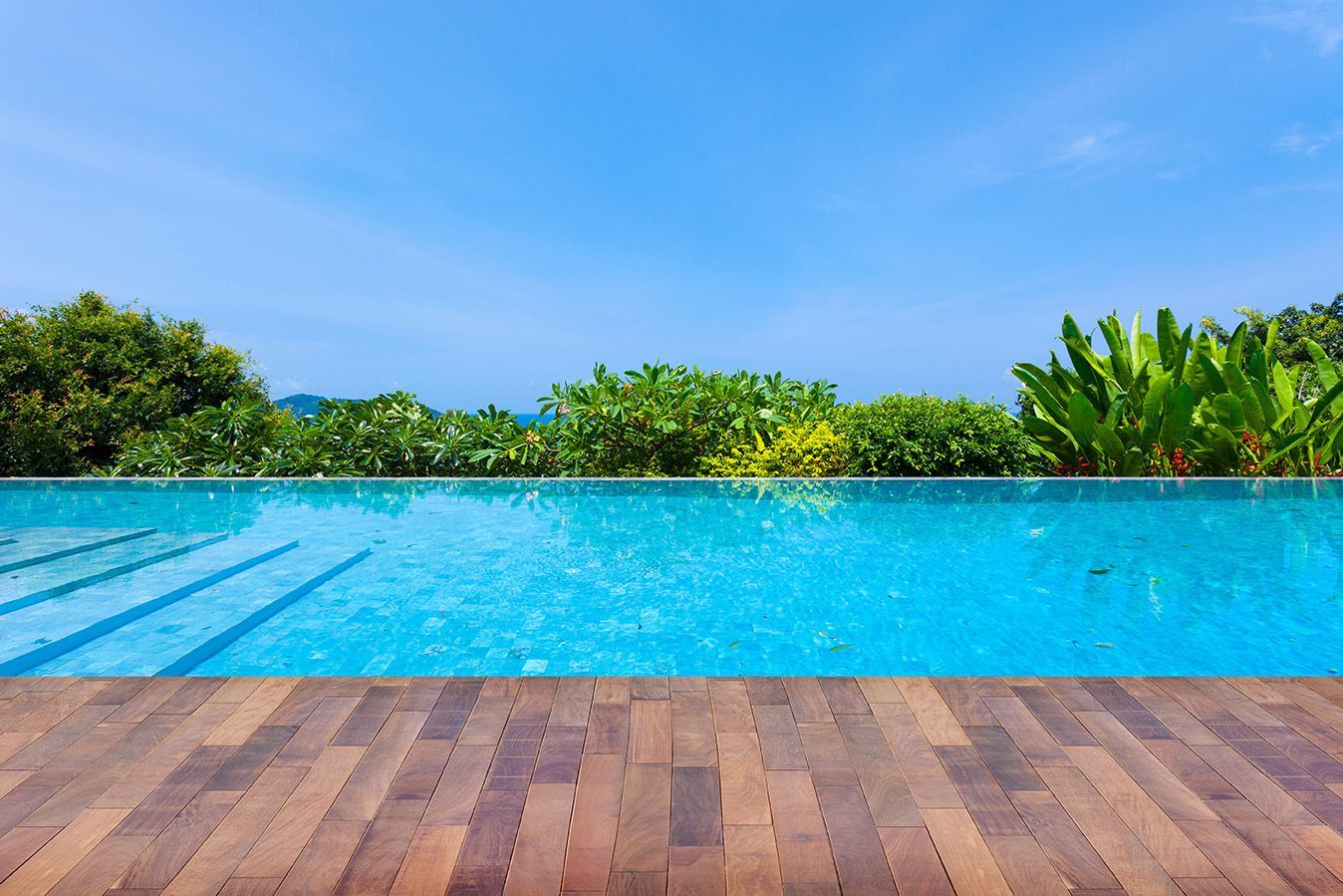 There is a swimming pool with a wooden deck in the foreground.