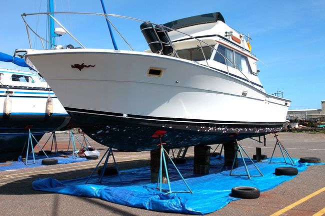 A white boat is sitting on a blue tarp in a parking lot.