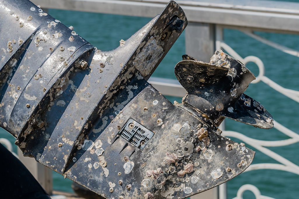 A dirty outboard motor is sitting on a railing next to the water.