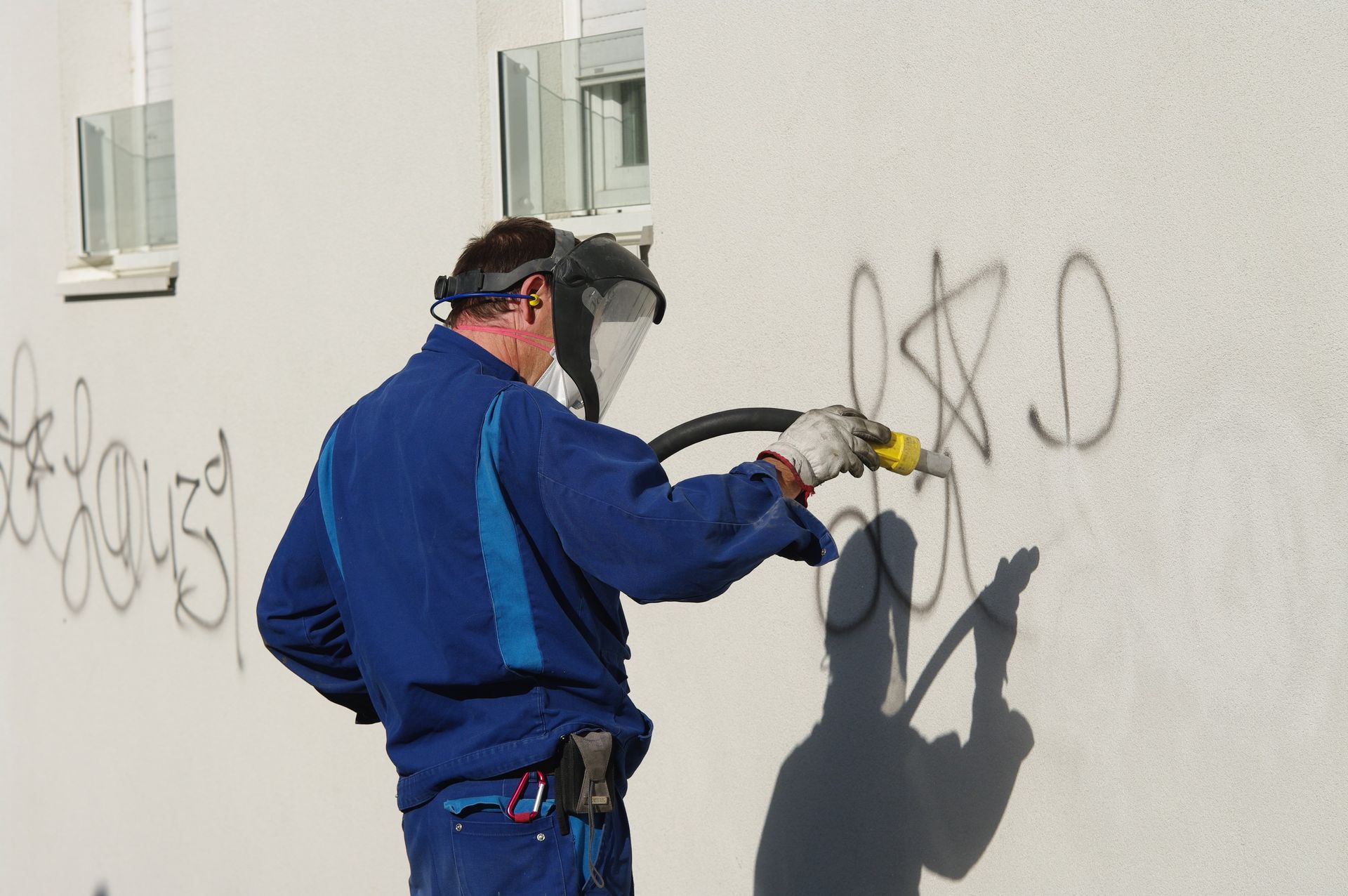 A man wearing a mask is cleaning graffiti on a wall.