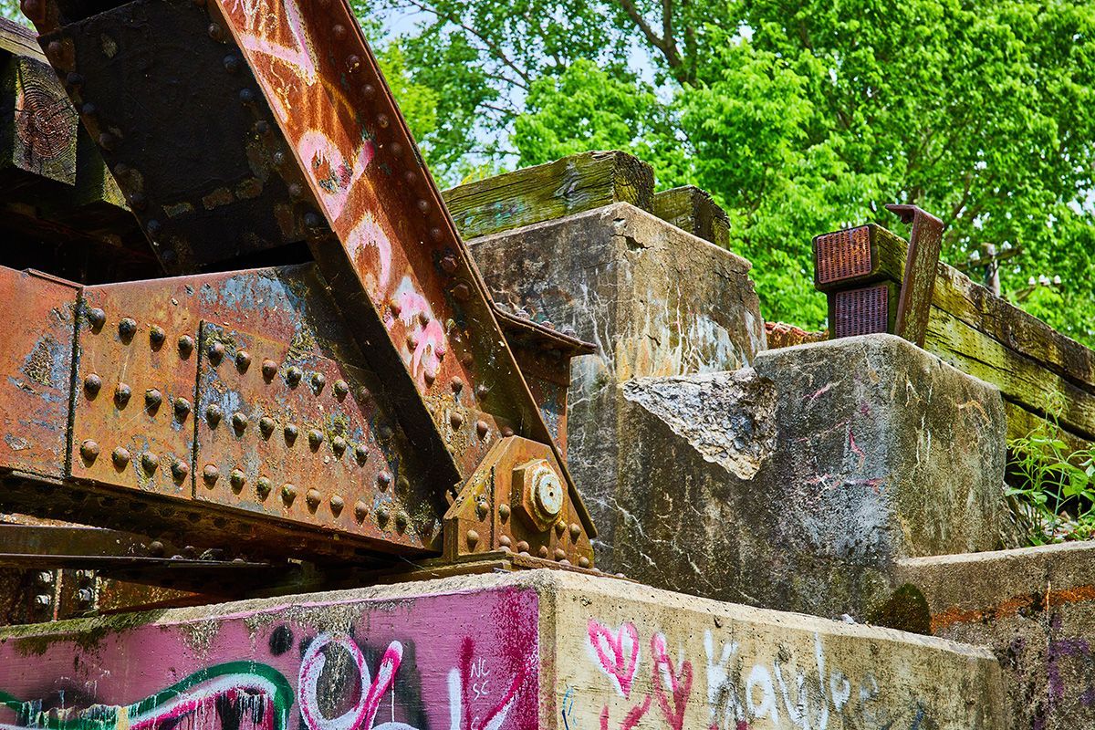 A rusty bridge with graffiti on it and trees in the background.