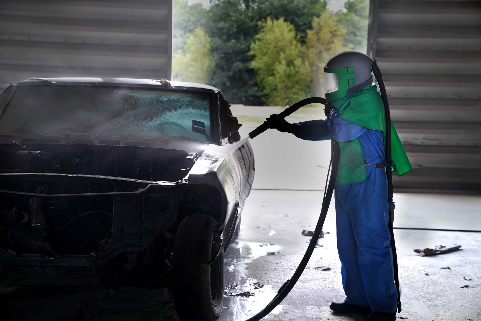 A man is sandblasting a car in a garage.