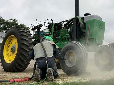 A man is kneeling in front of a green tractor.