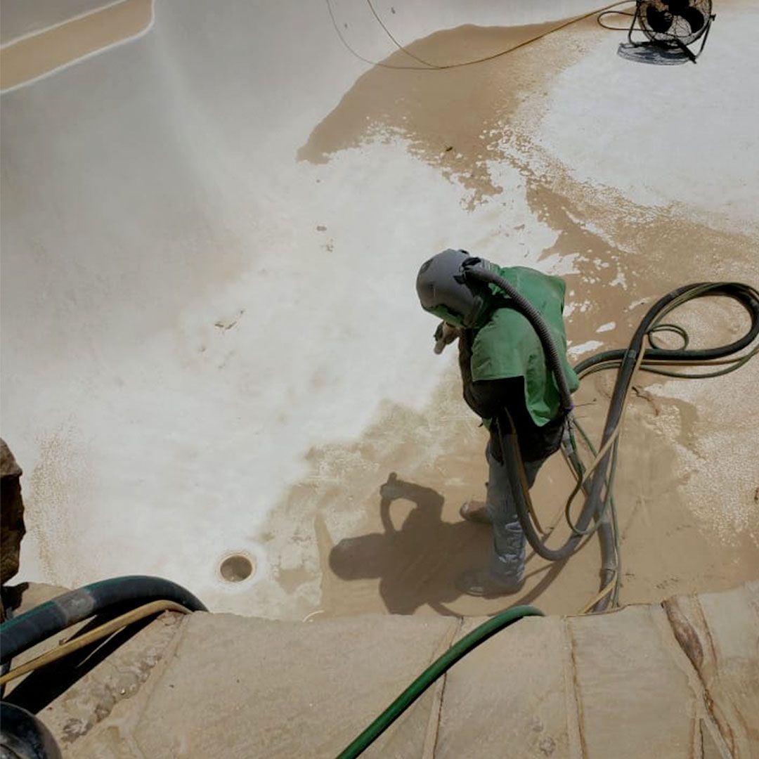 A man wearing a green shirt is sandblasting a pool