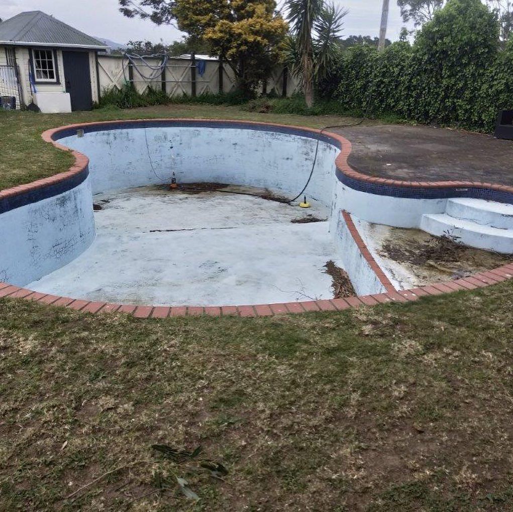 An empty swimming pool in a backyard with a house in the background