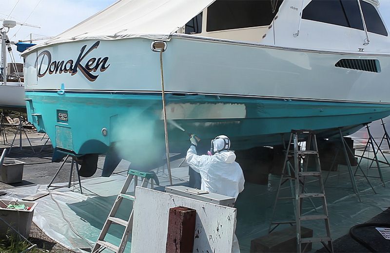 A man in a white suit is painting a boat.