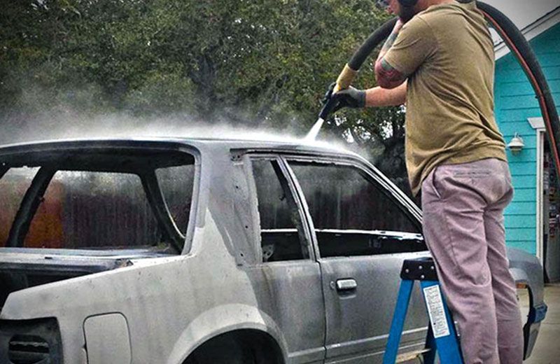 A man is cleaning a car with a high pressure washer.