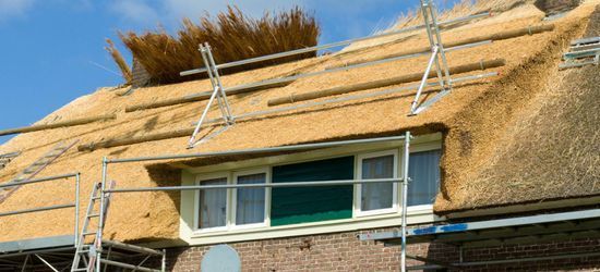 Een rieten dak op een bakstenen gebouw met witte kozijnen en steigers.