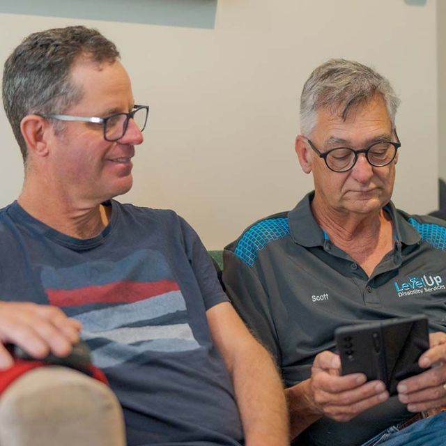two men are sitting on a couch looking at a phone .