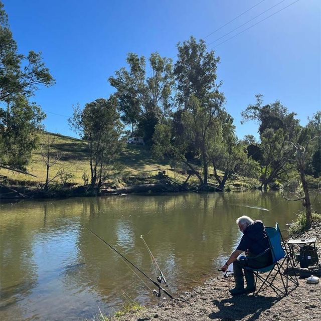 a man is sitting on the shore of a lake fishing .