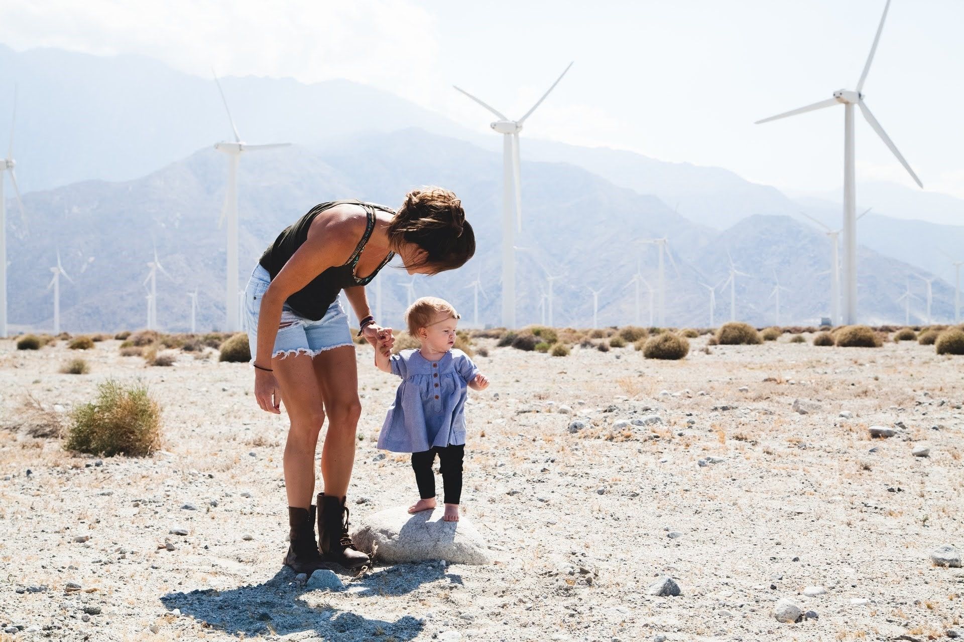 A woman and a little girl are playing in the desert with wind turbines in the background.