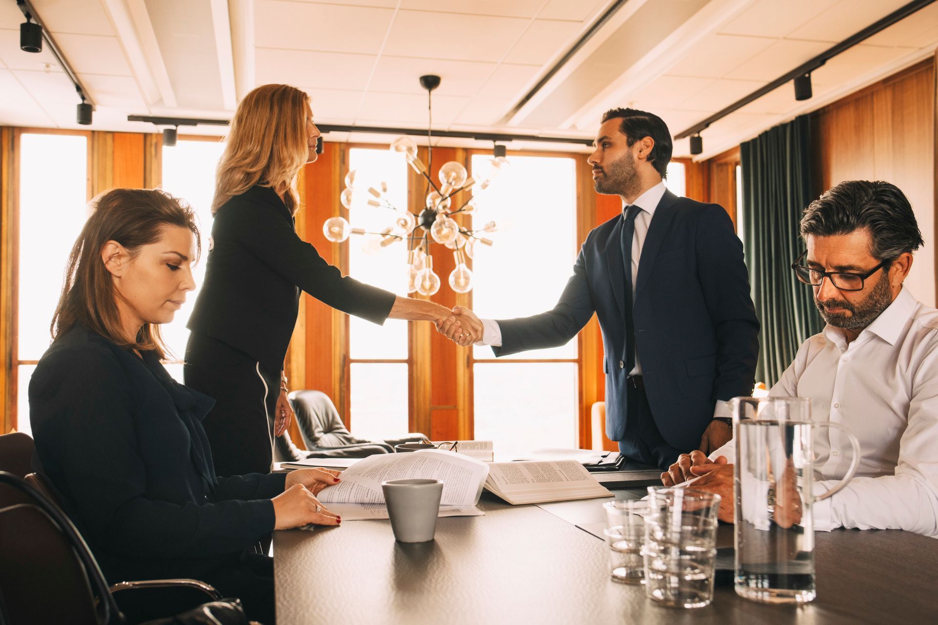 Two lawyers shaking hands while their clients sit at a table during a divorce meeting