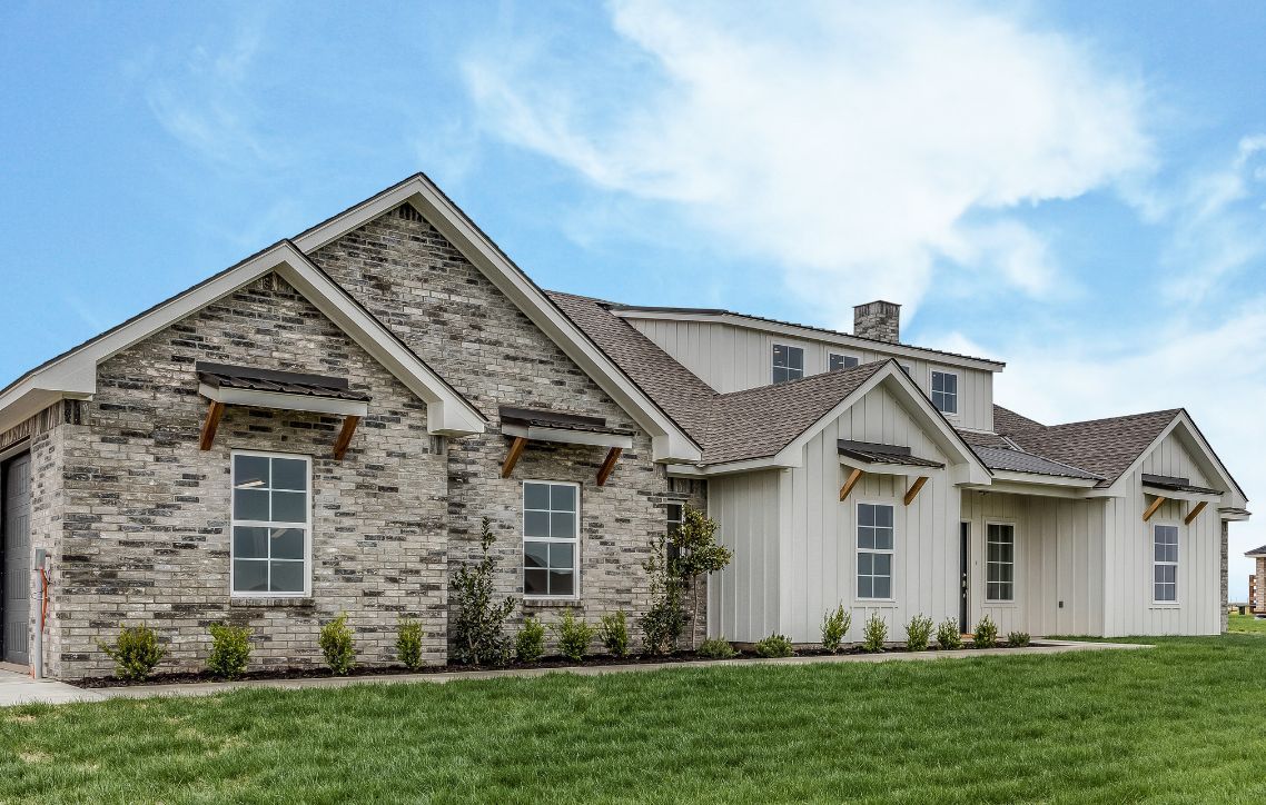 A large house with a lot of windows is sitting on top of a lush green field.
