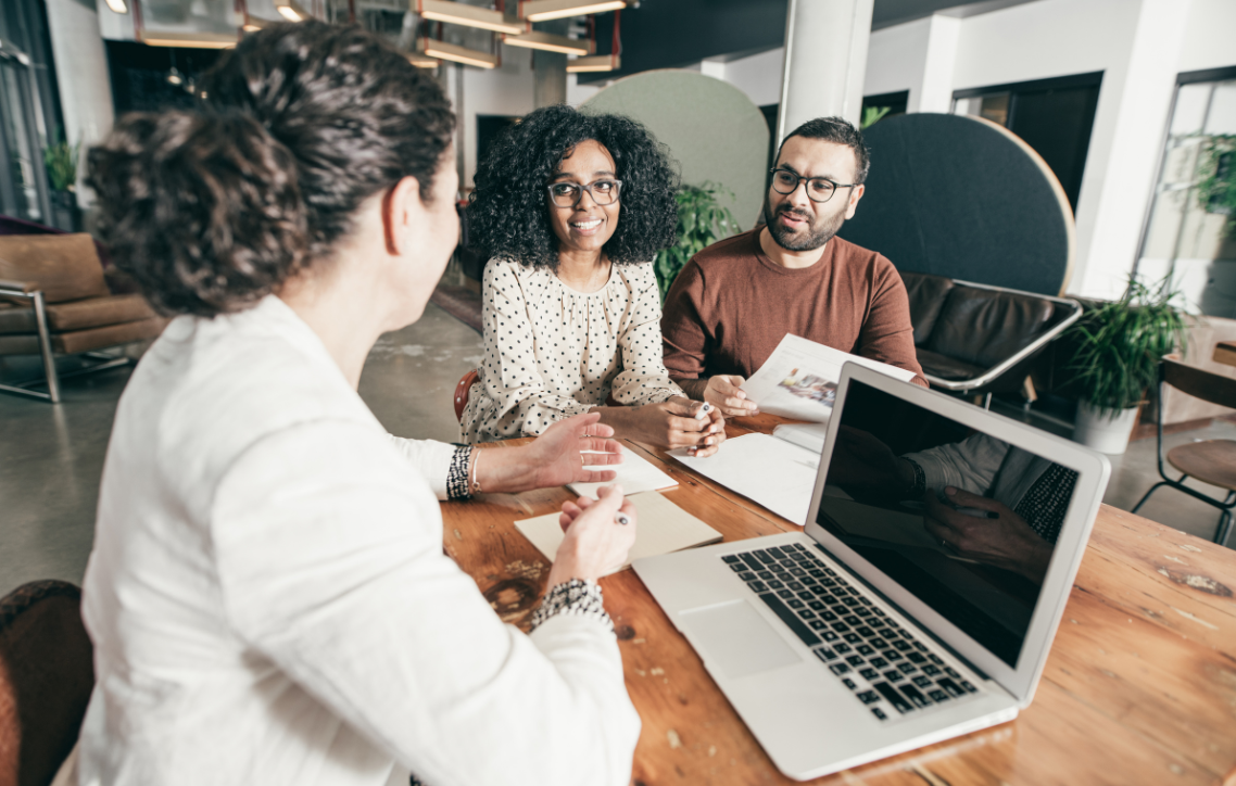 A man and a woman are sitting at a table with a laptop.