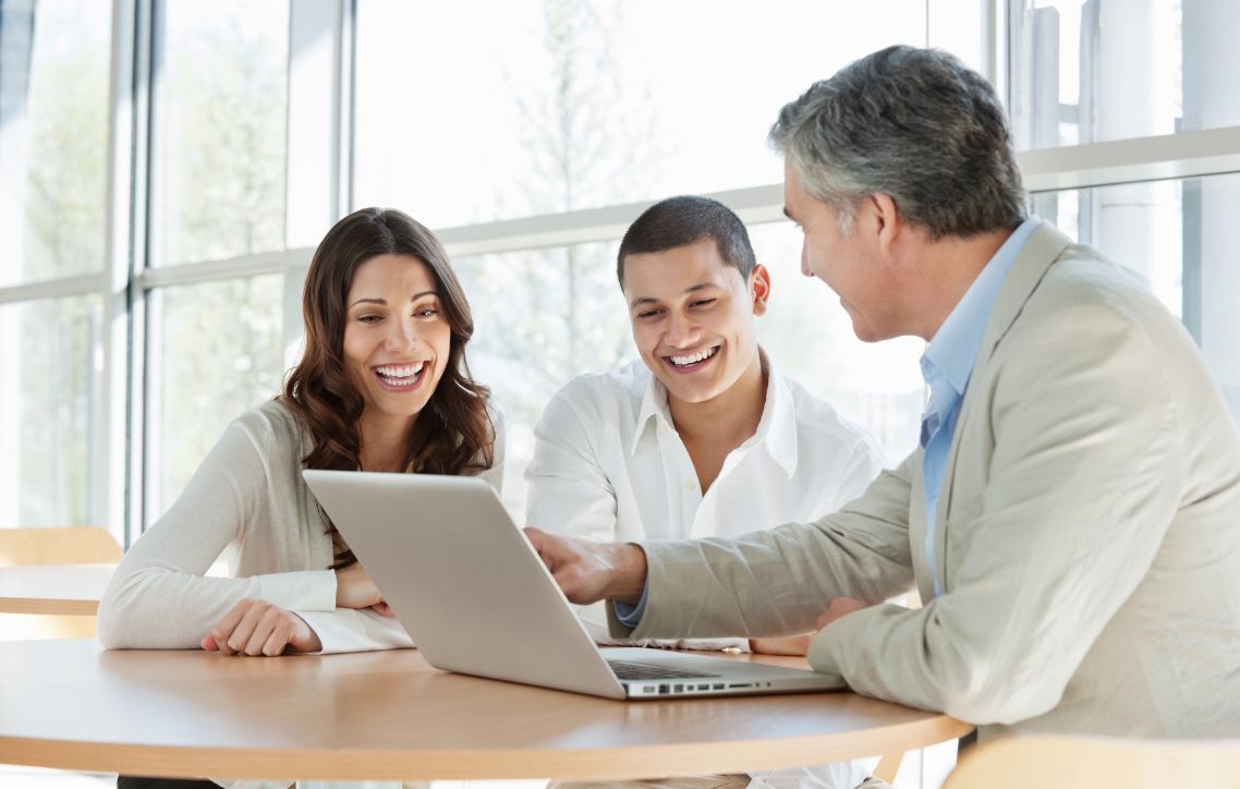 A man and a woman are sitting at a table looking at a laptop.