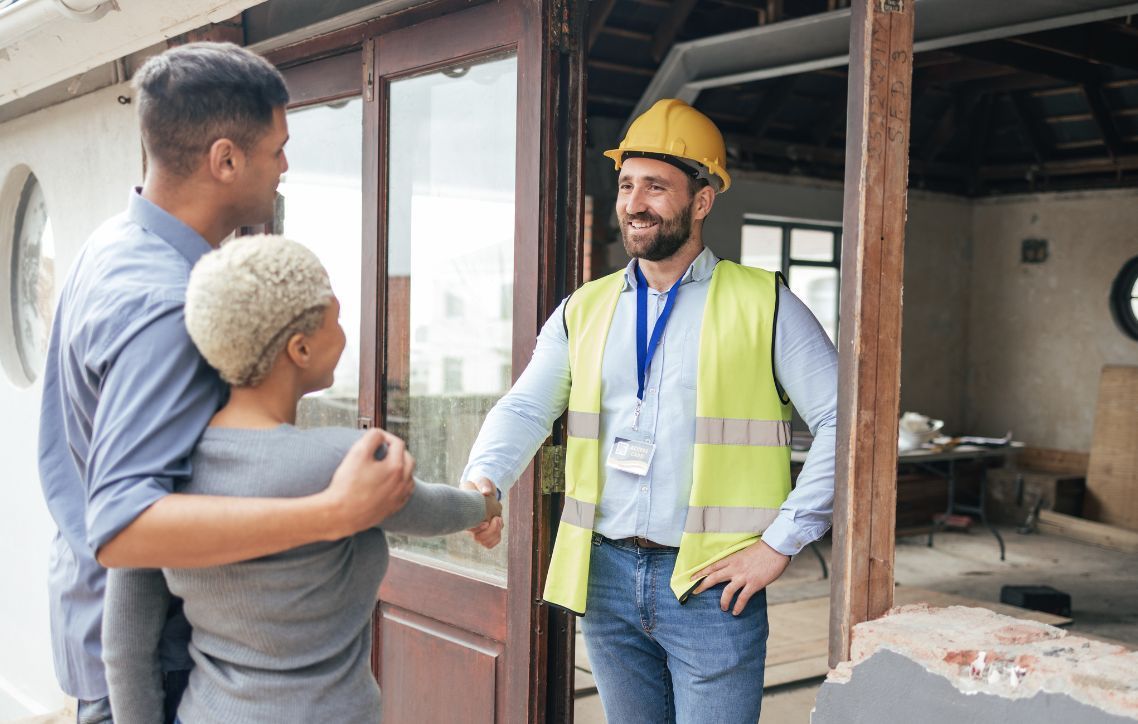 A man in a hard hat is shaking hands with a woman and a man.