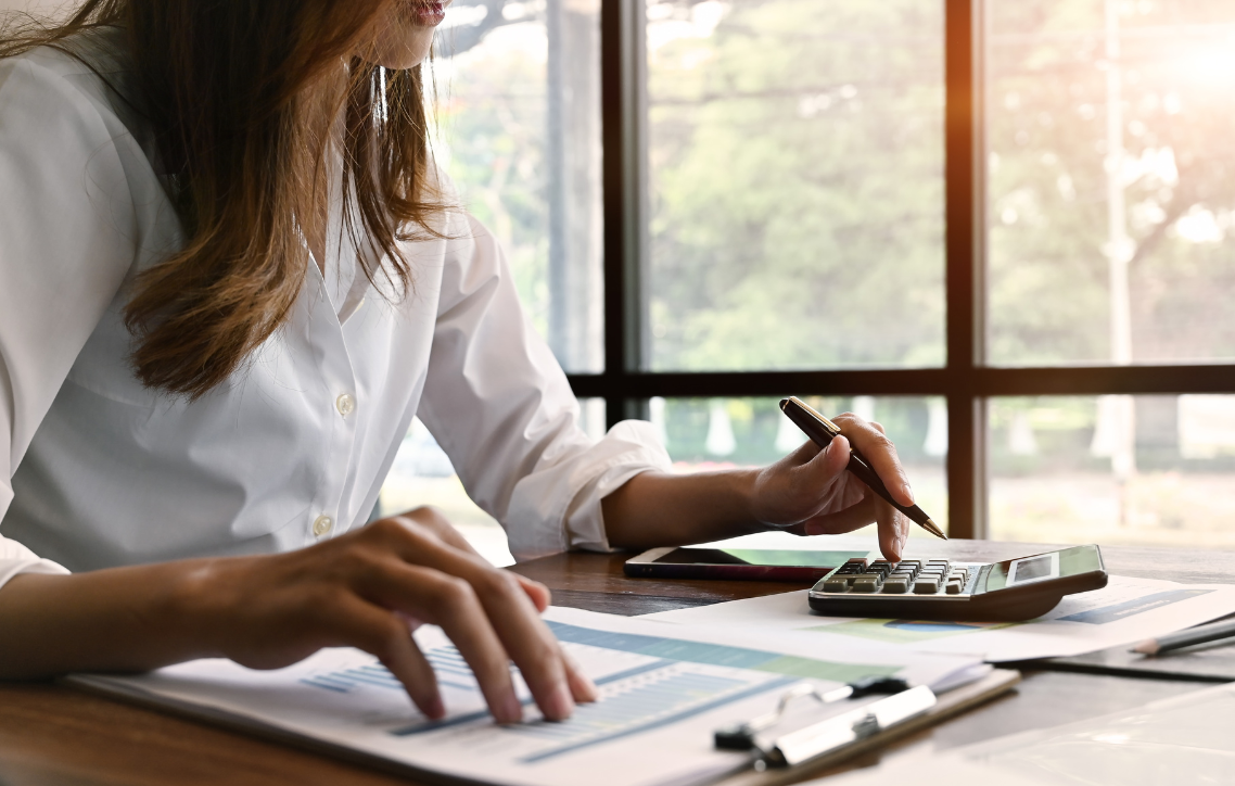A woman is sitting at a desk using a calculator and a pen.