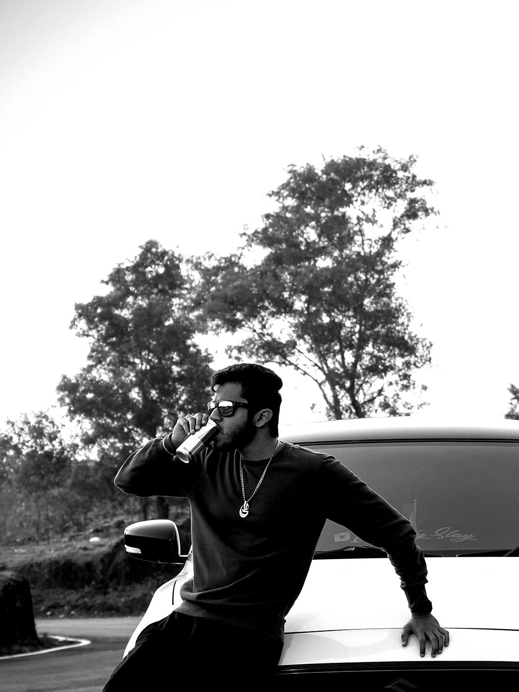 A man is sitting on the hood of a car talking on a cell phone.