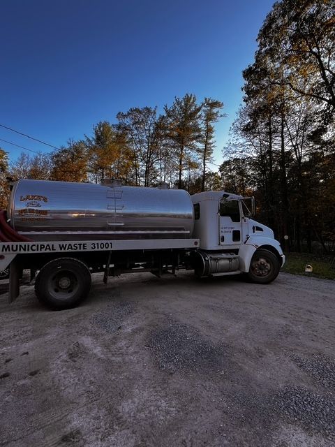 A white septic truck parked on gravel, with a shiny silver tank, under a blue sky. A white septic truck parked on gravel, with a shiny silver tank, under a blue sky.