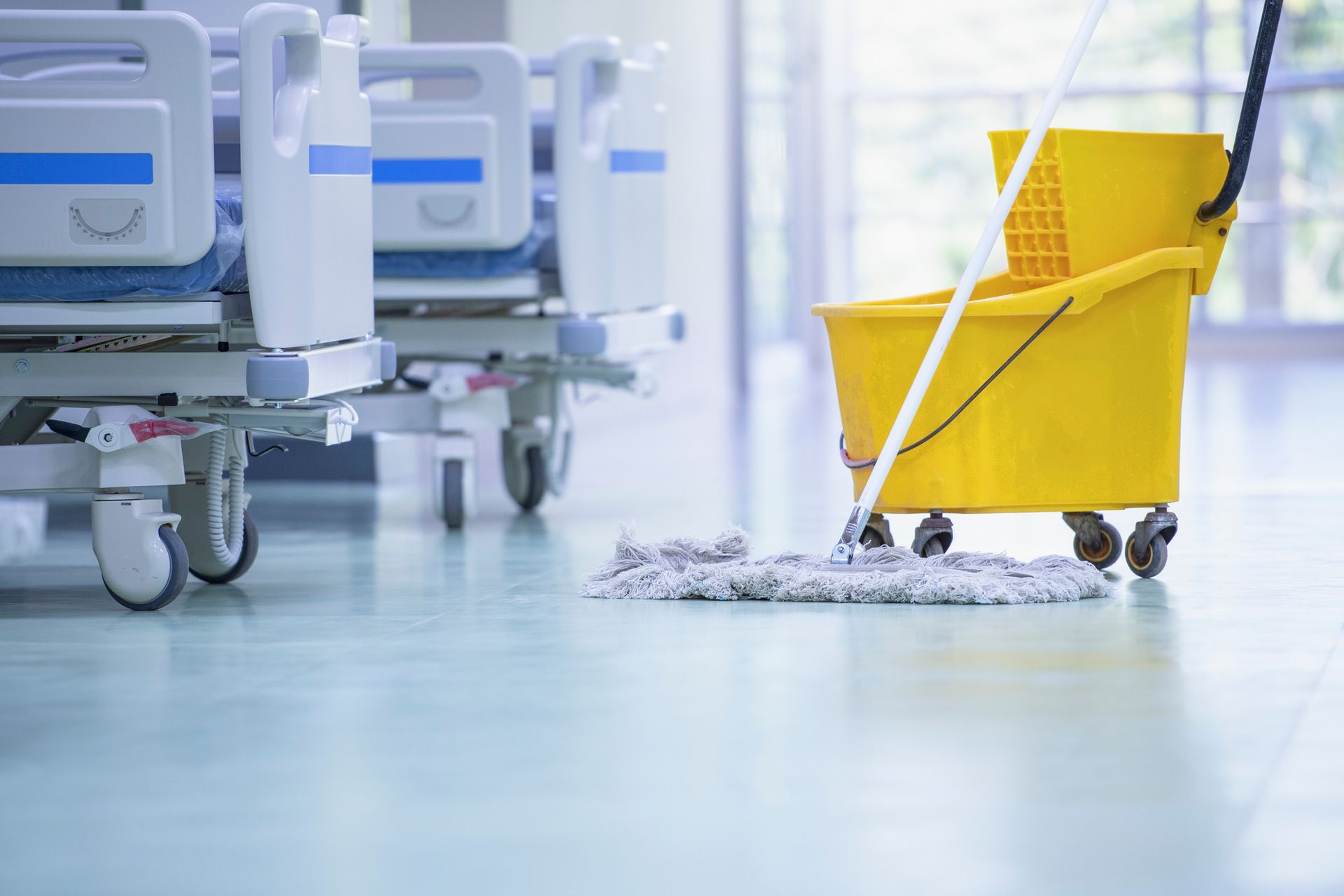 Hospital floor being mopped with a yellow bucket and mop beside hospital beds