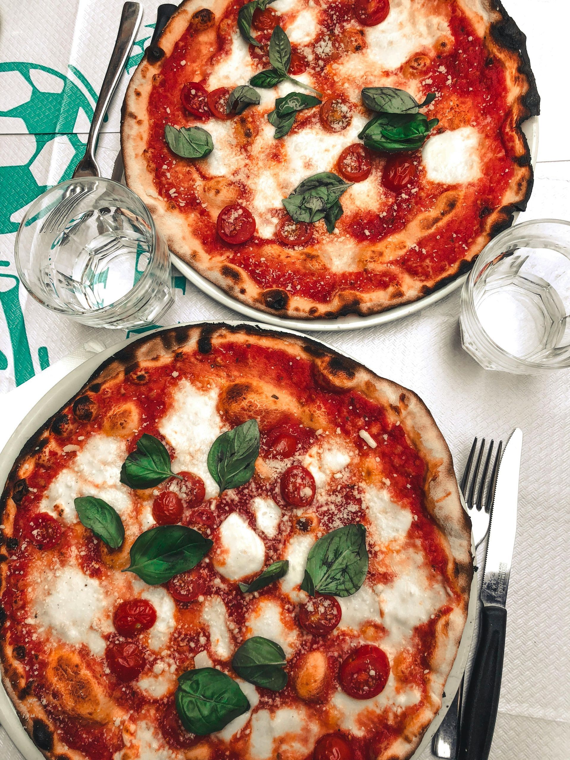 Two pizzas with tomatoes and basil on them on a table