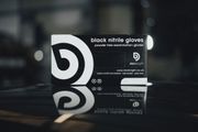 Black nitrile gloves box on a reflective surface with a spiral logo, in a dimly lit setting.