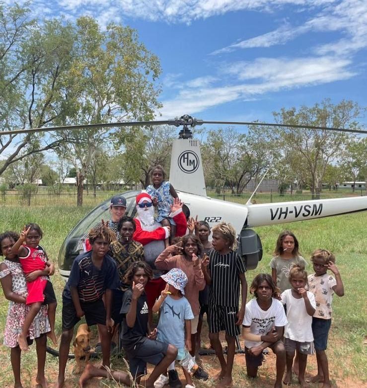 Santa Claus with children in front of a helicopter in a sunny outdoor setting.